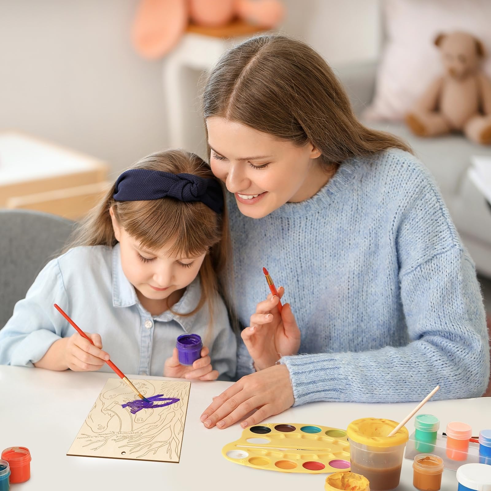 Woman and child painting unfinished wood Halloween ornaments at a table with paints and brushes