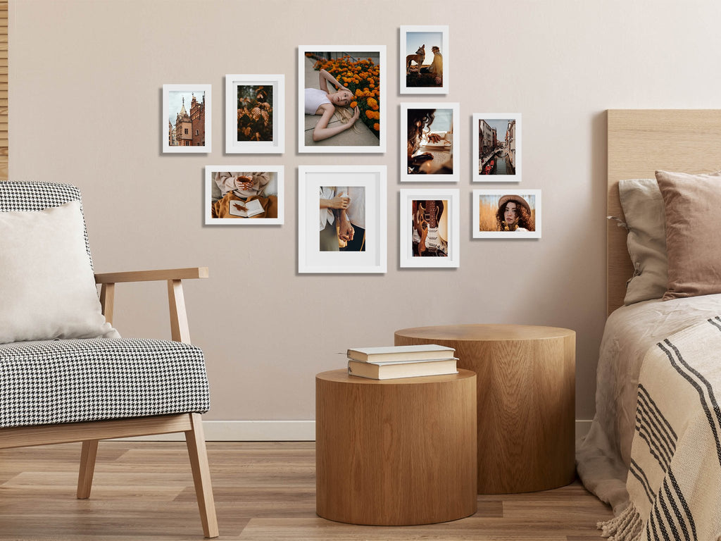 Gallery wall of ten white picture frames arranged on a wall above a chair and bedside tables, showcasing various lifestyle images.