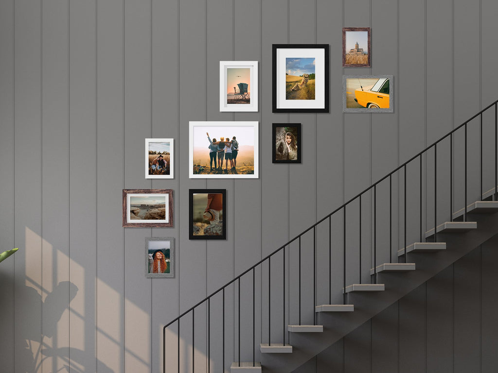 Gallery wall of picture frames arranged on a grey paneled wall next to a staircase