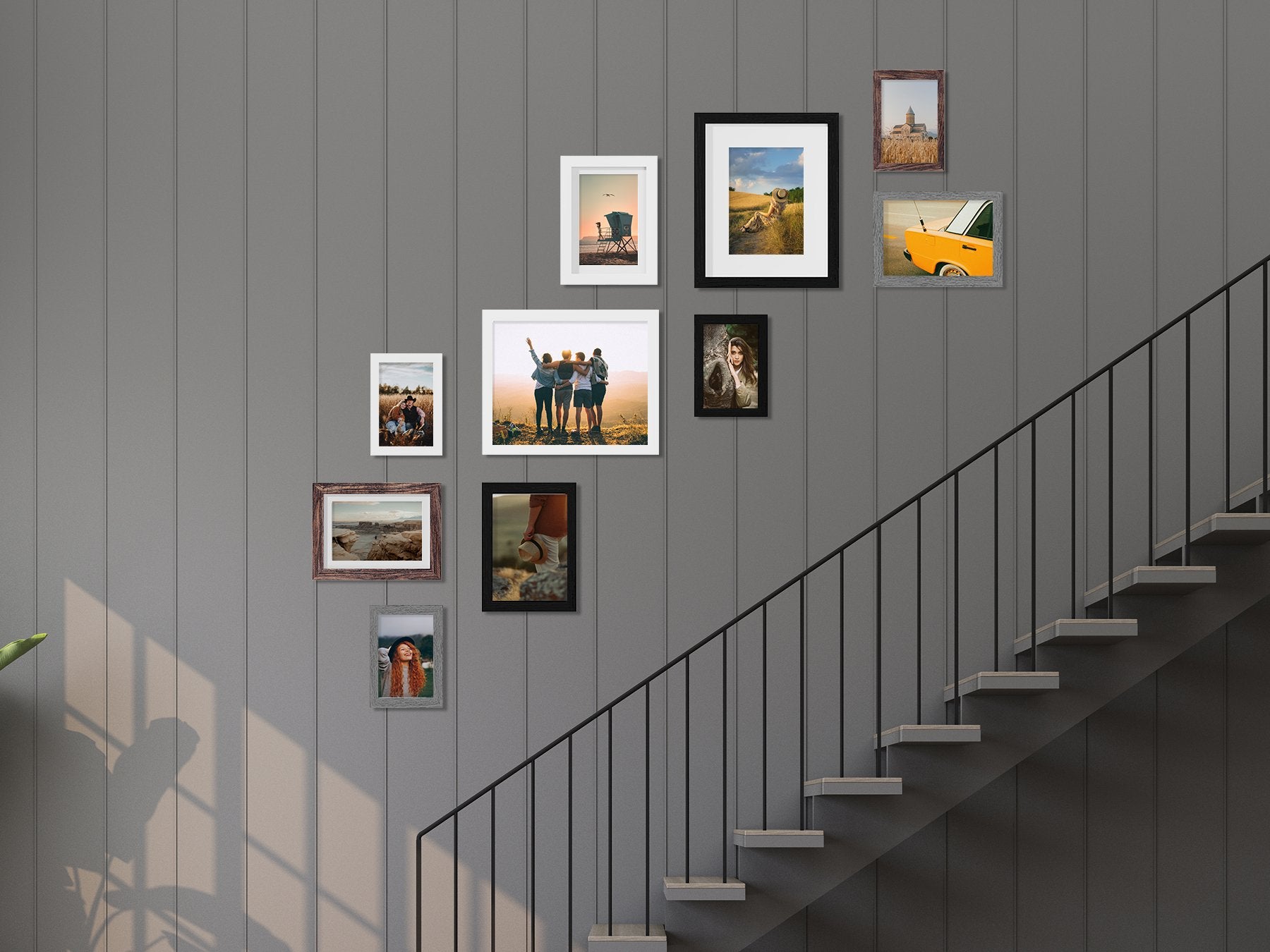 Gallery wall of picture frames arranged on a grey paneled wall next to a staircase