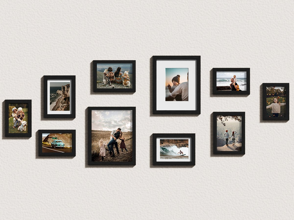 Gallery wall arrangement of ten black picture frames displaying various family and scenic photos on a textured white wall.