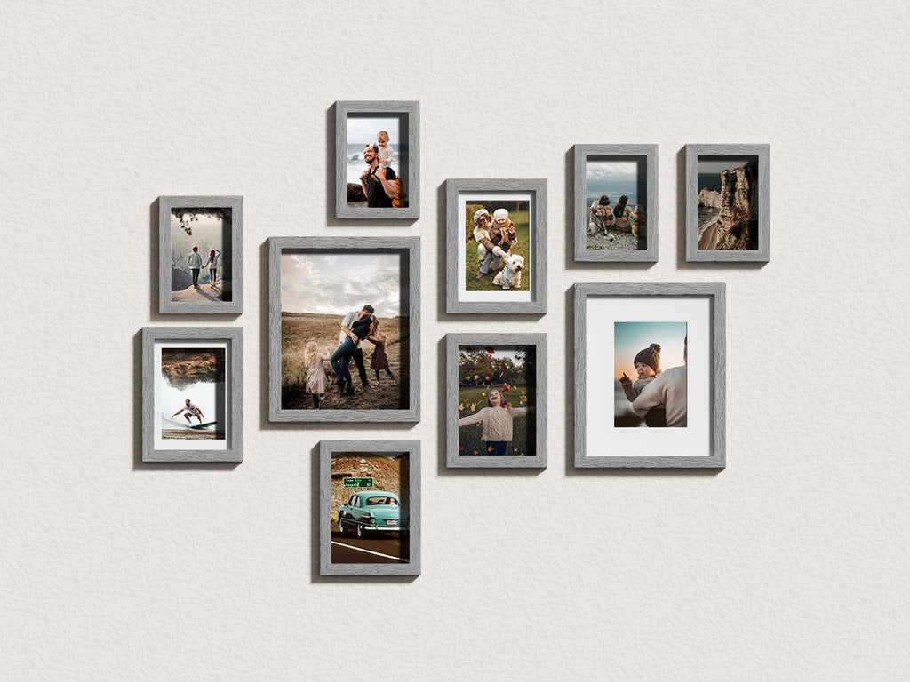 Gallery wall arrangement of ten grey picture frames displaying various family photos and scenic shots on a textured white wall.