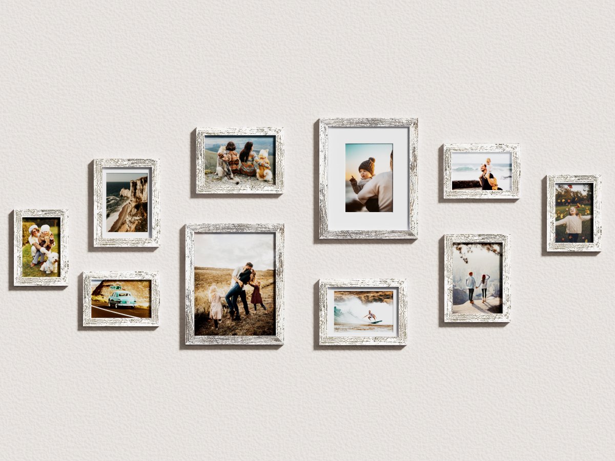 Gallery wall of ten distressed white wood picture frames displaying various family photos and scenic shots on a textured wall.