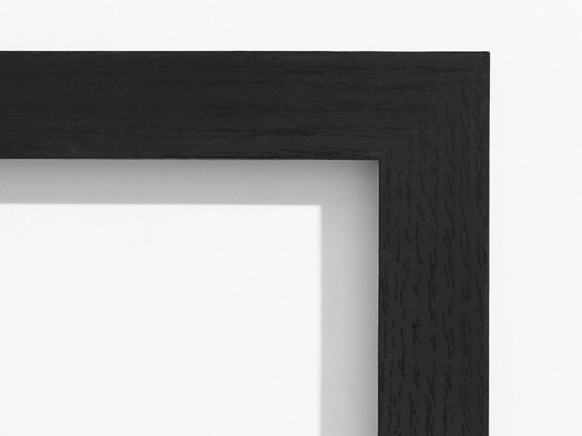 Close-up of a black engineered wood picture frame corner with a white matting visible inside.