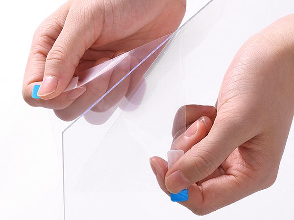 Hands peeling protective film off clear acrylic sheet for picture frame
