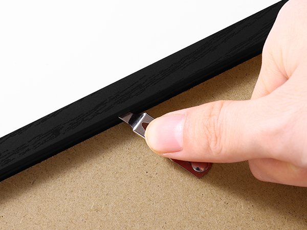 Close-up of a hand using a tool to secure a backing clip on a black picture frame.
