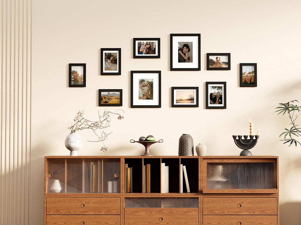 Gallery wall of ten black picture frames arranged above a wooden credenza with decorative items.