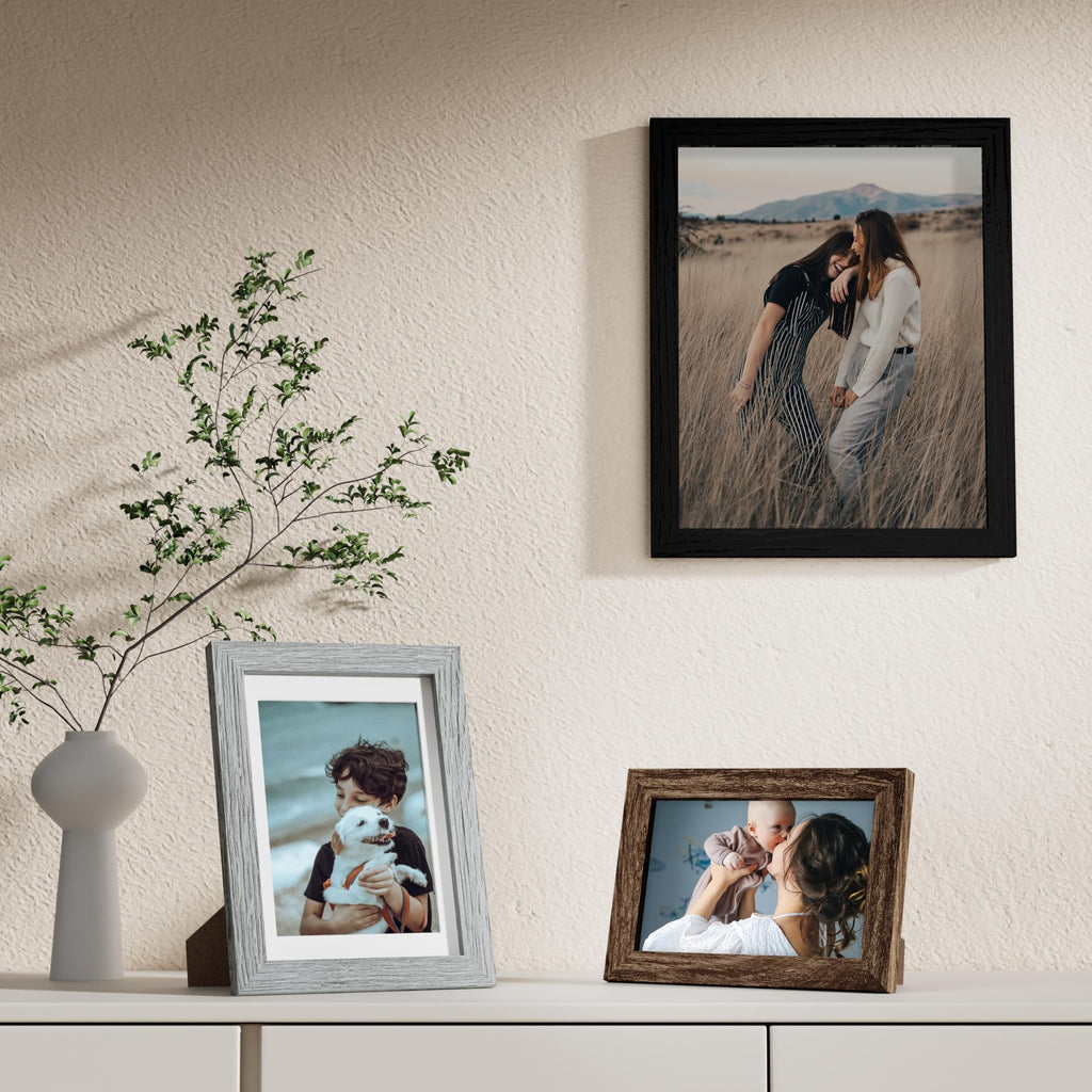 Three picture frames displayed on a shelf with a vase and plant.