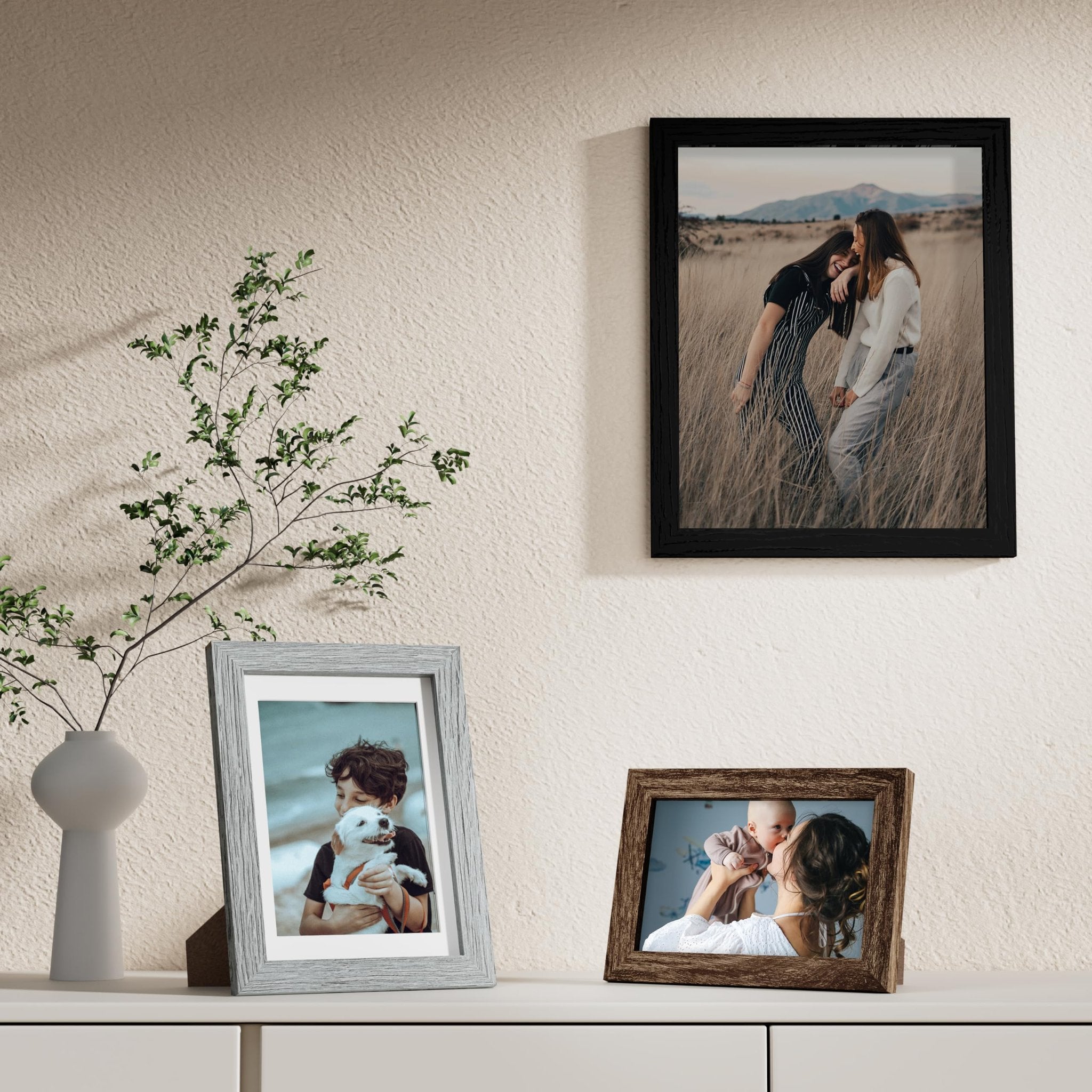 Three picture frames displayed on a shelf with a vase and plant.
