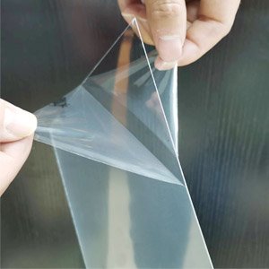 Hands peeling protective film off a clear plastic sheet