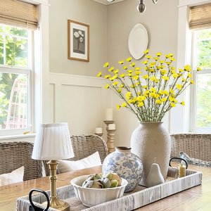 Yellow wildflowers in a vase on a wooden table with a lamp and decorative bowl.