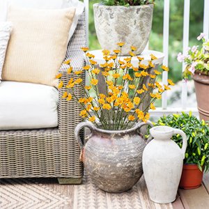 Yellow wildflowers in a rustic vase on a patio next to outdoor furniture and potted plants.