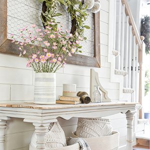 Vase of pink forsythia branches on a console table with a wreath and staircase in the background.