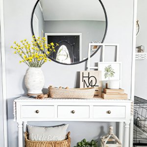 Yellow wildflowers in a vase on a console table with decorative items and a mirror above