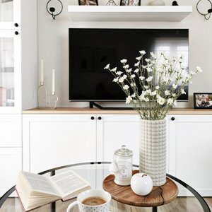 White artificial forsythia flowers in a textured vase on a coffee table with an open book and coffee cup.