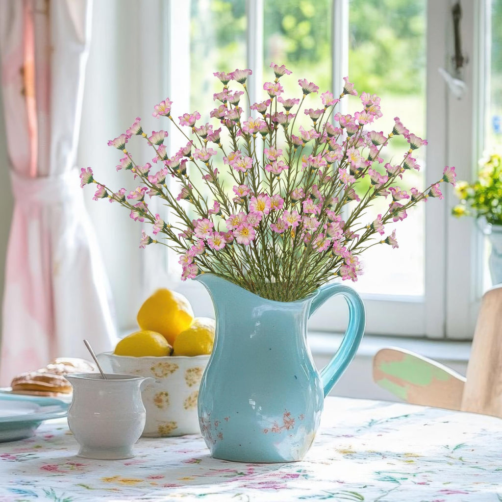 Bouquet of artificial pink forsythia branches in a light blue pitcher on a table with lemons and pastries