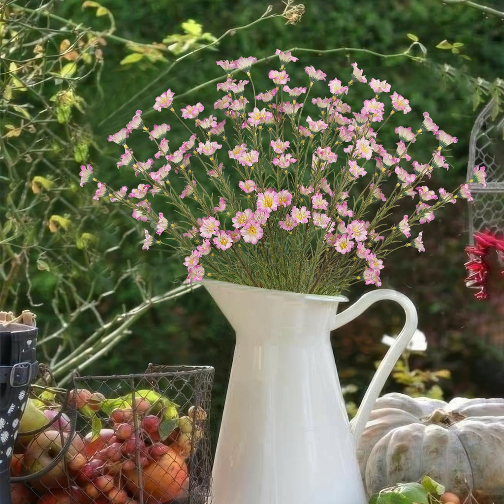 White pitcher filled with pink forsythia branches, next to a basket of apples and a pumpkin.