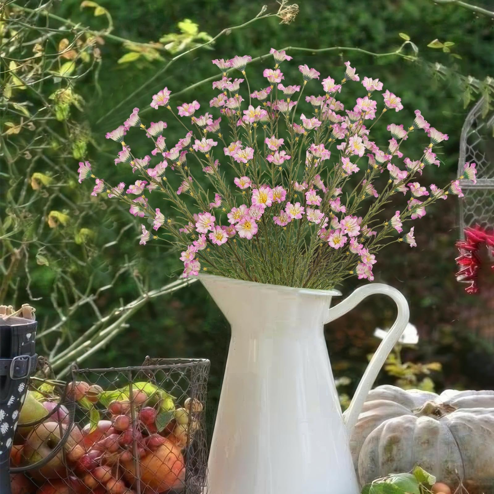 White pitcher filled with pink forsythia branches, next to a basket of apples and a pumpkin.