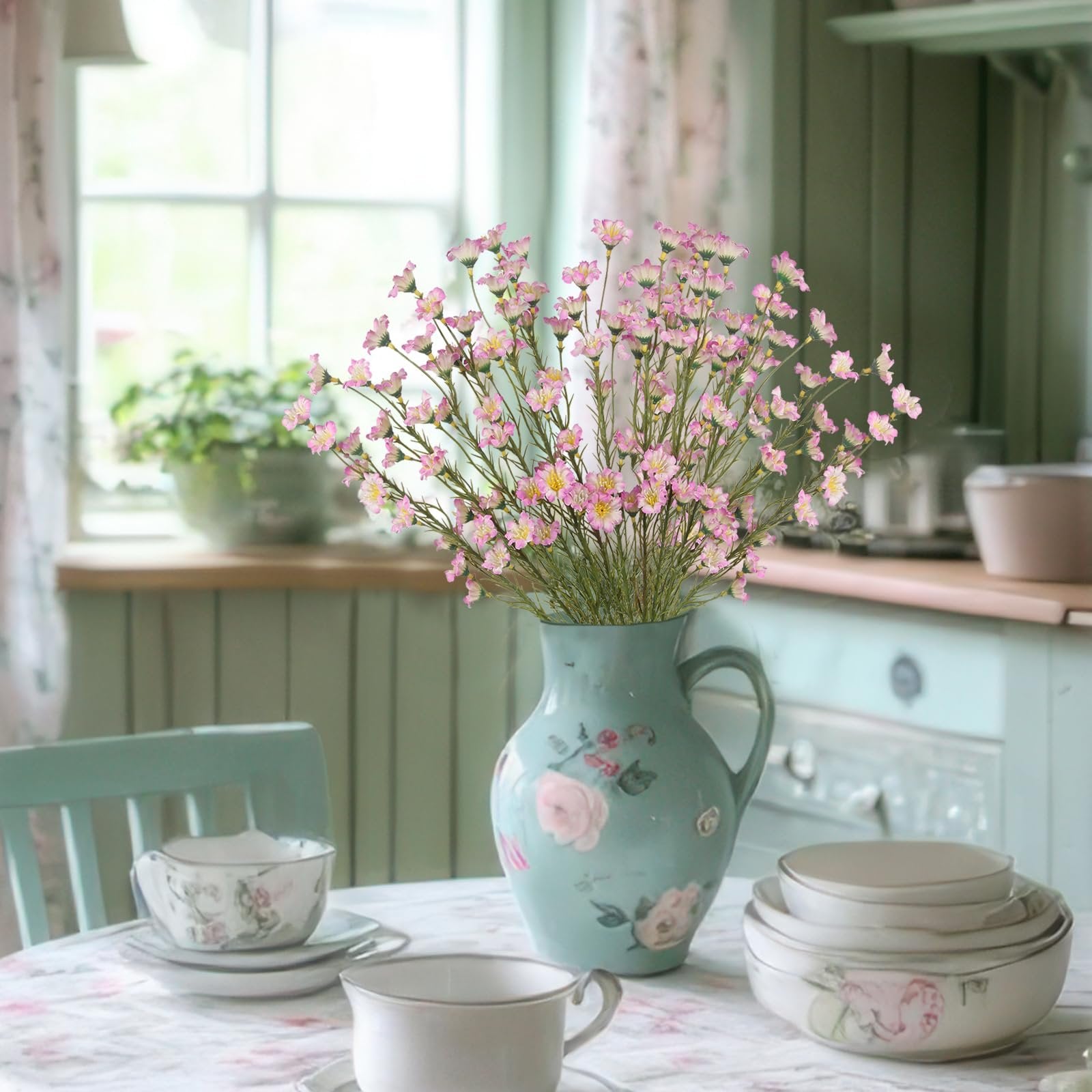 Bouquet of pink wildflowers in a decorative vase on a table with teacups and bowls