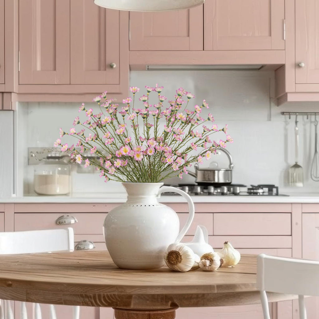 Artificial pink forsythia branches in a white vase on a wooden table with garlic and a kitchen background