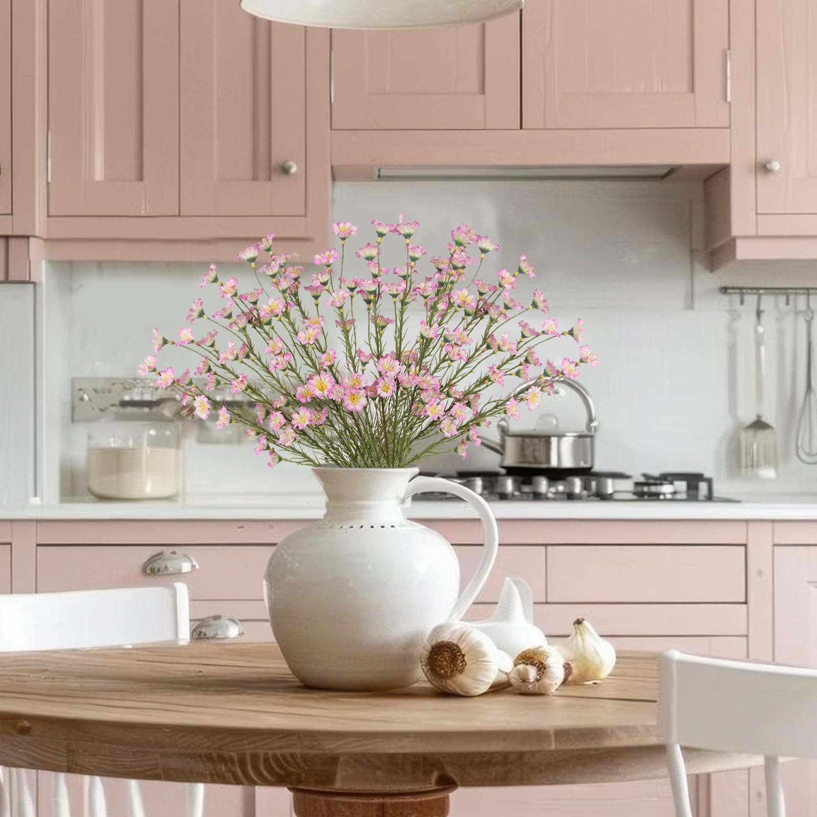 Artificial pink forsythia branches in a white vase on a wooden table with garlic and a kitchen background
