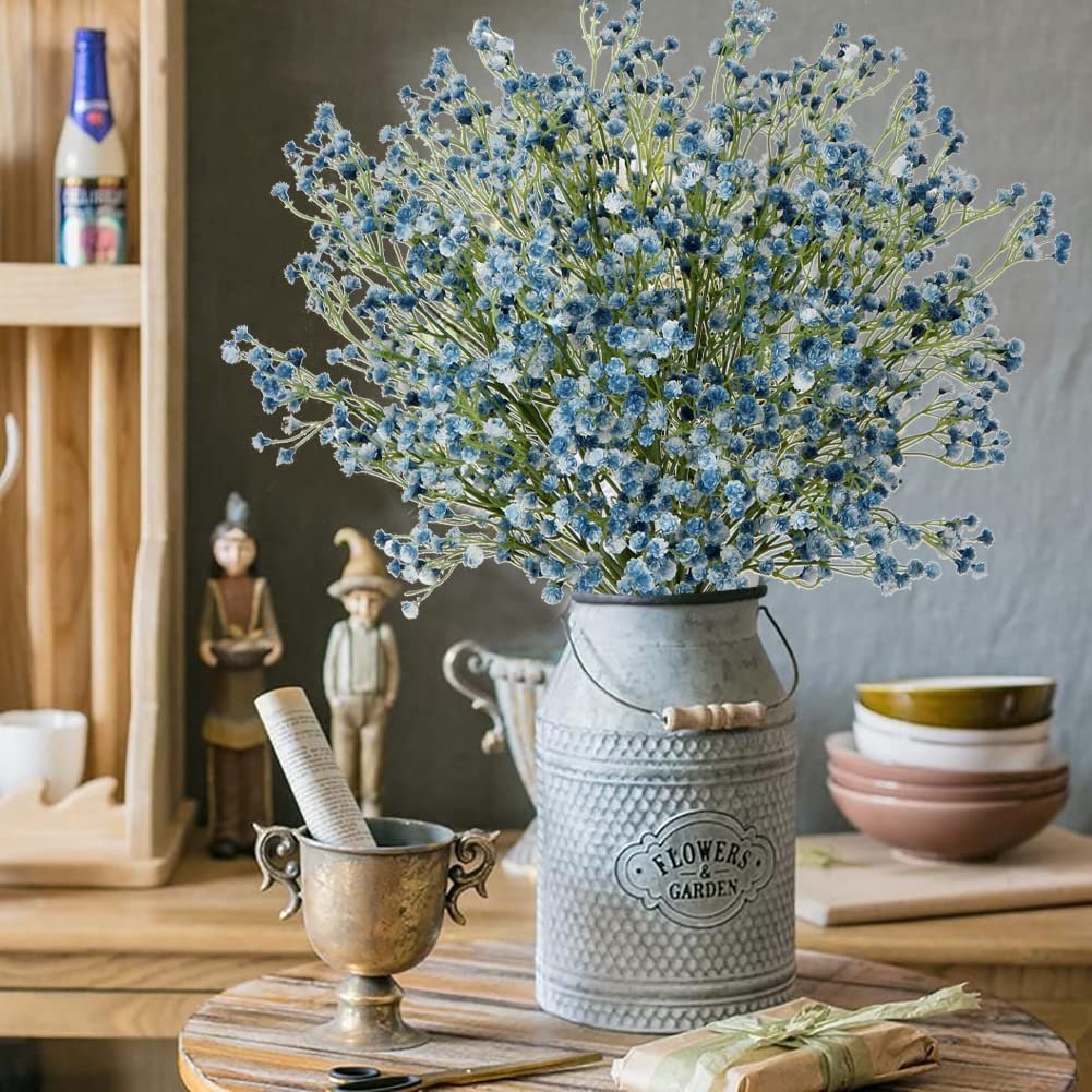 Blue artificial baby's breath flowers in a rustic metal vase on a wooden table, with decorative figures and bowls in the background.