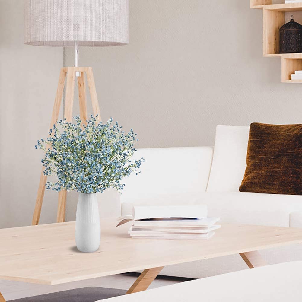 Blue artificial baby's breath flowers in a white vase on a wooden coffee table in a living room setting.