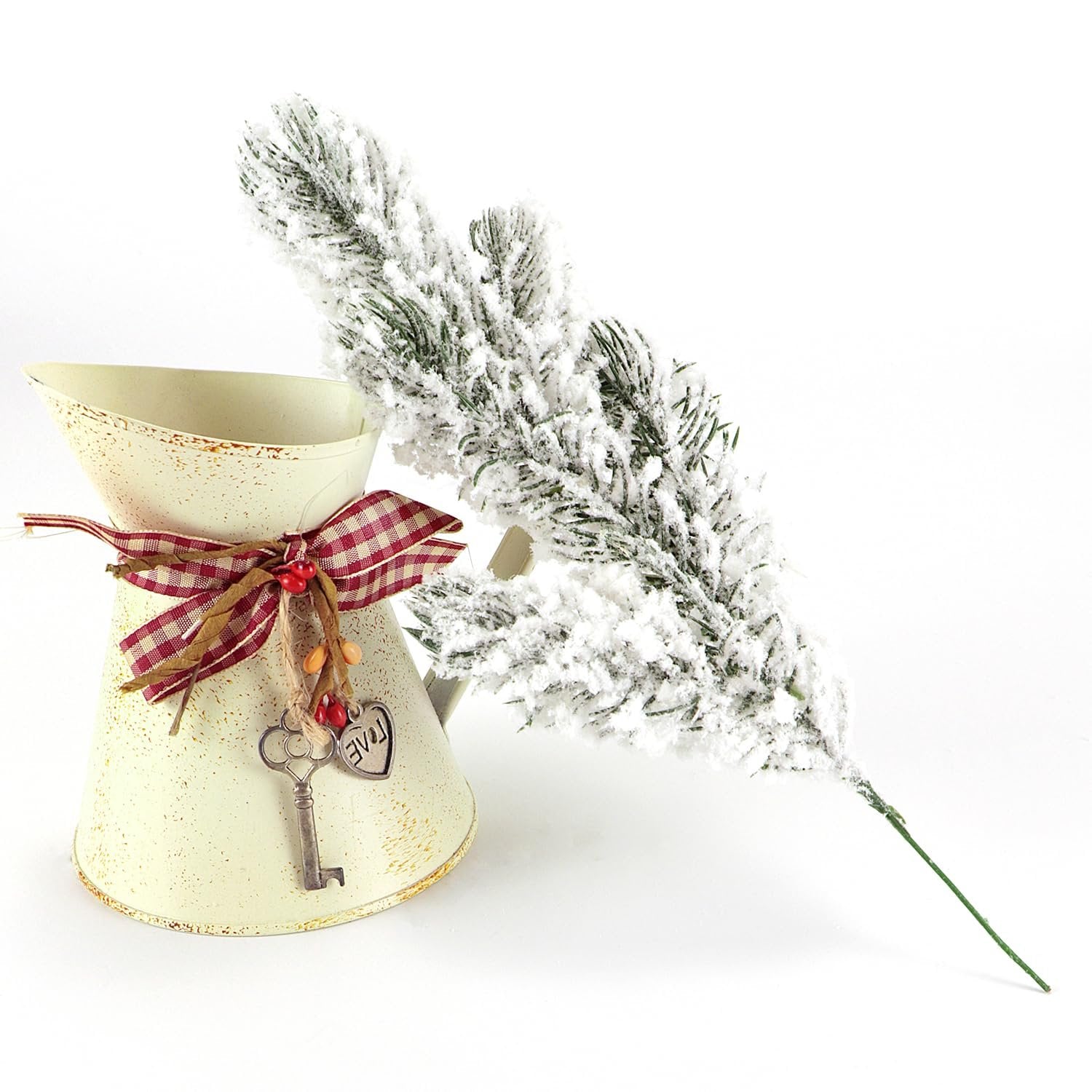 Frosted artificial pine branch next to a decorative metal pitcher with a checkered ribbon and a key charm.