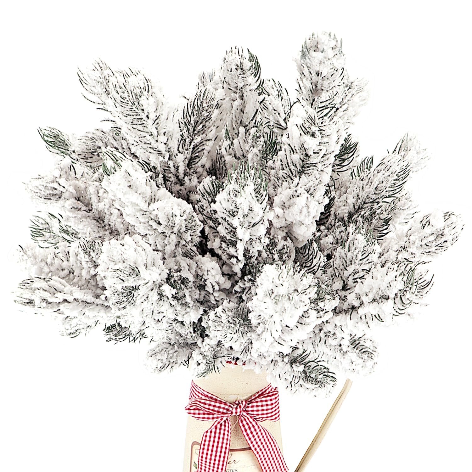 Frosted artificial pine needle branches with white snow in a decorative vase with a red and white checkered ribbon.