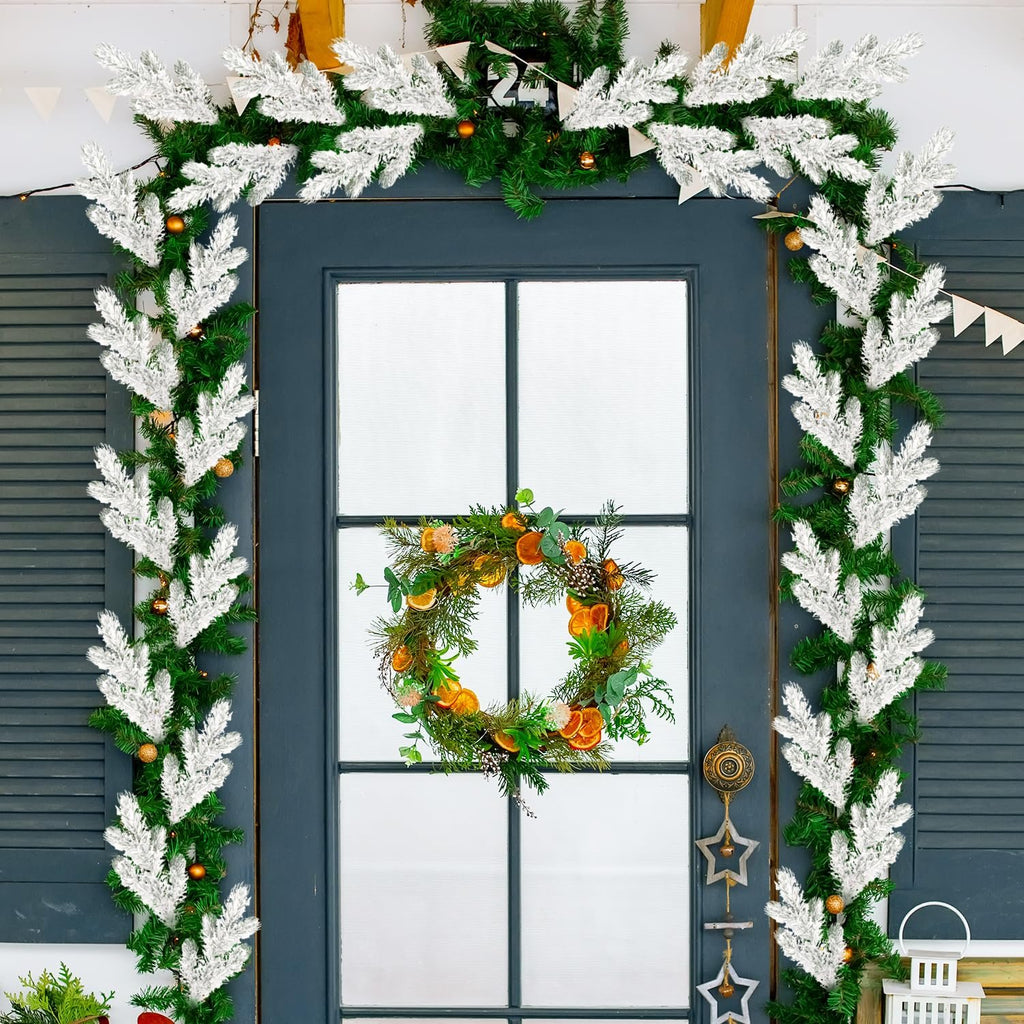 Frosted artificial pine needle branches and a wreath decorating a dark blue door for Christmas.