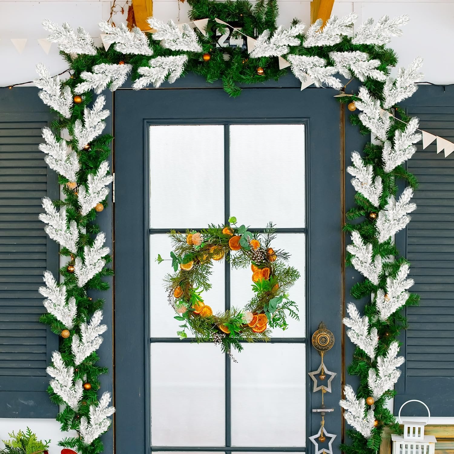 Frosted artificial pine needle branches and a wreath decorating a dark blue door for Christmas.
