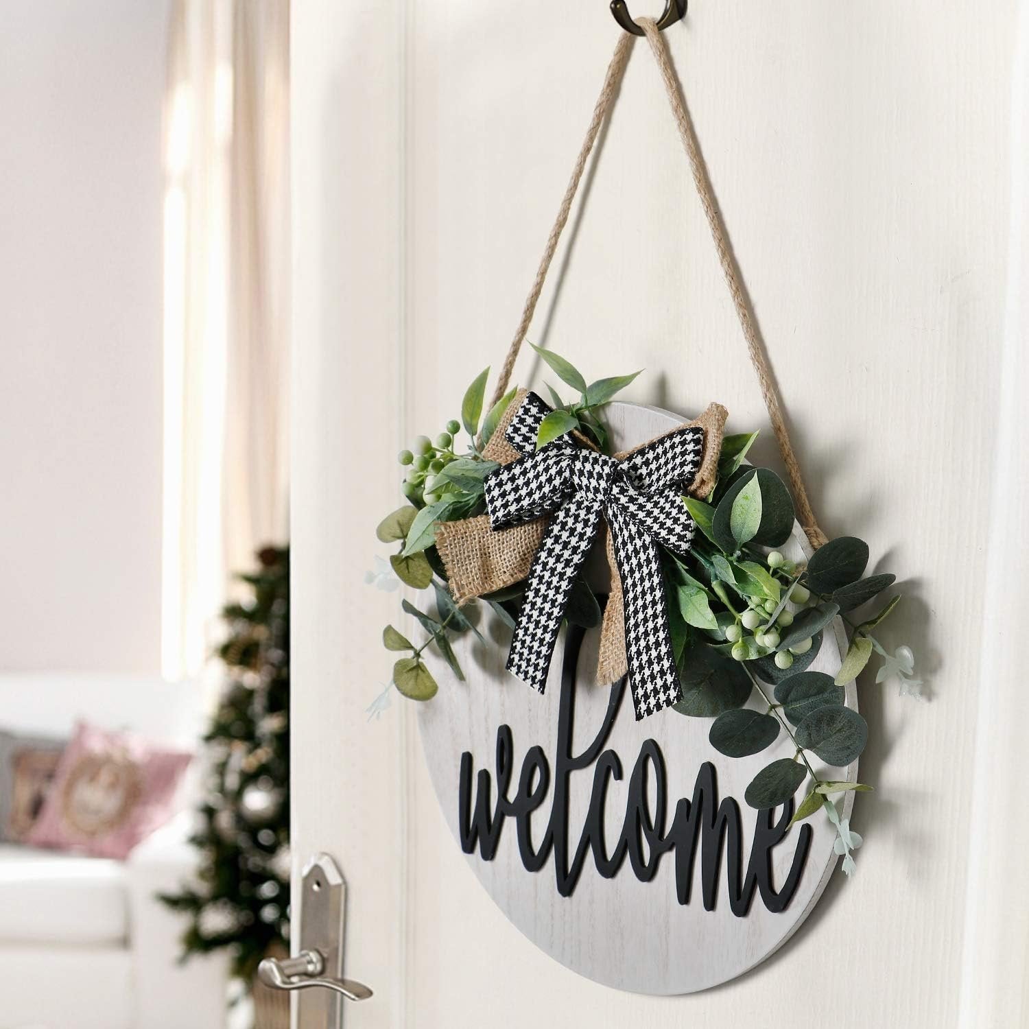 Round wooden welcome sign with faux greenery and a black and white bow hanging on a door.