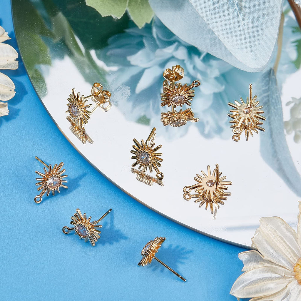 Gold plated sun-shaped earring findings with cubic zirconia and loops, displayed on a reflective surface.