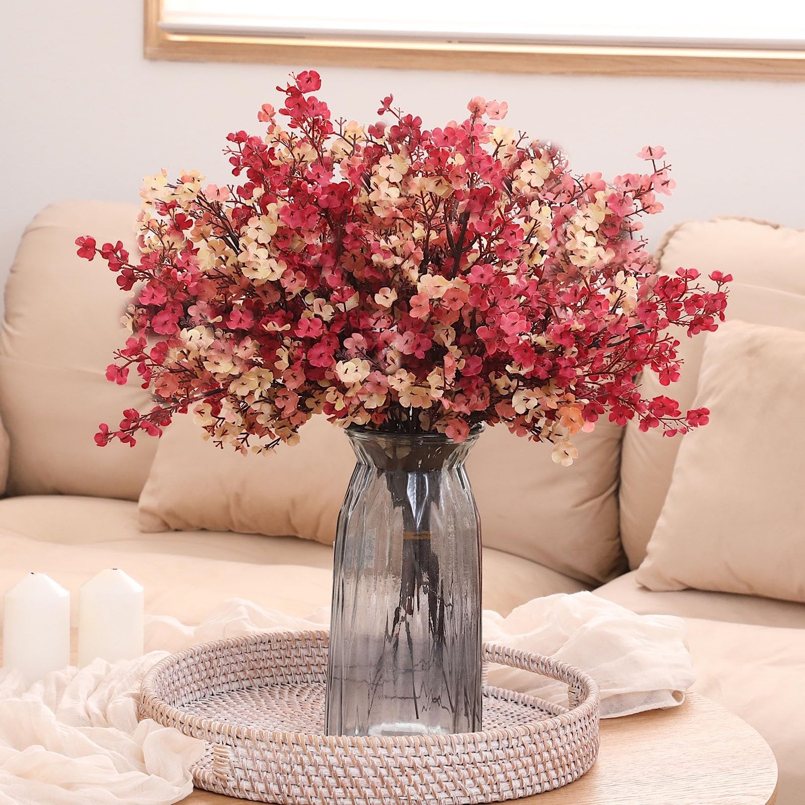 Bouquet of artificial baby's breath flowers in coffee and burgundy colors in a glass vase on a tray with candles.
