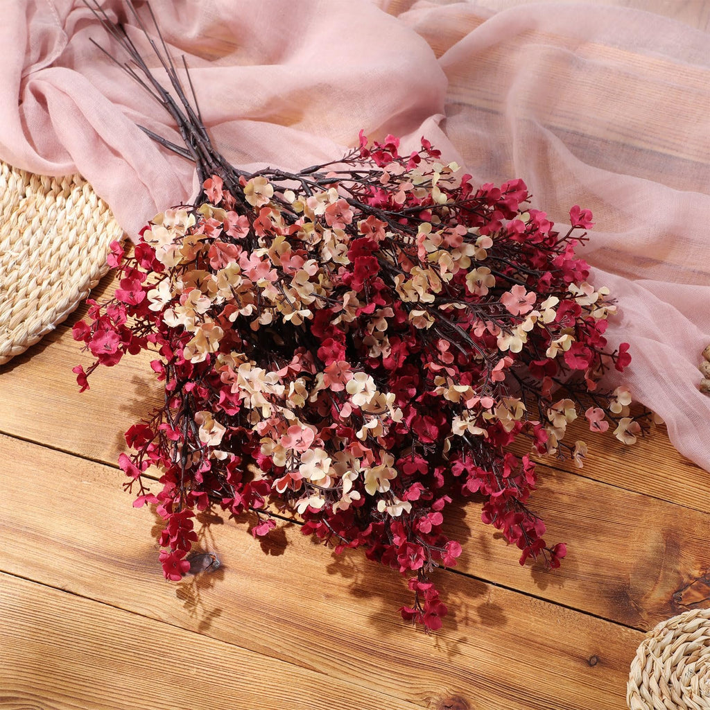 Bouquet of artificial baby's breath flowers in coffee and burgundy colors on a wooden surface with pink fabric.