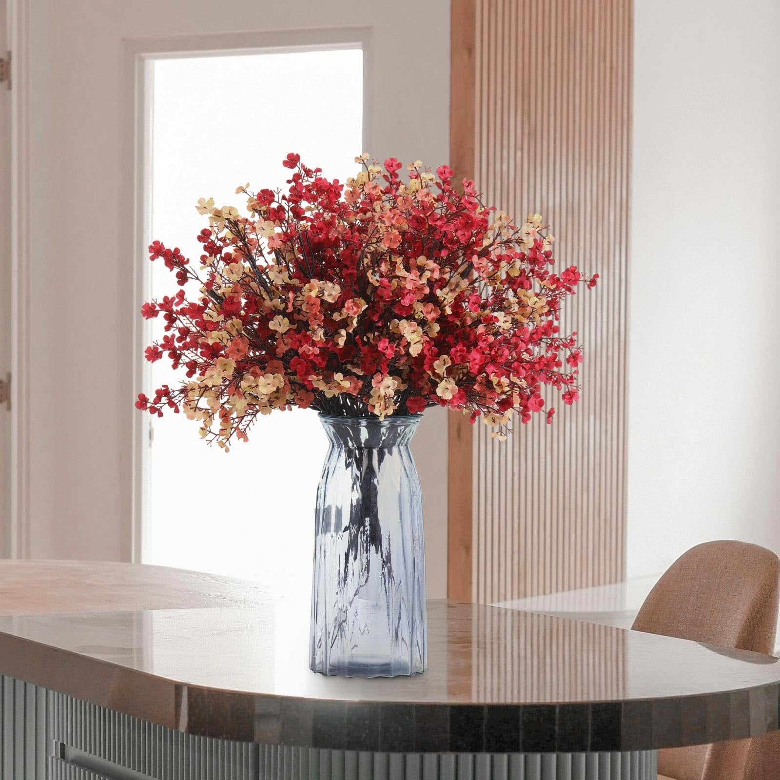 Bouquet of artificial baby's breath flowers in red and yellow hues in a blue glass vase on a table.