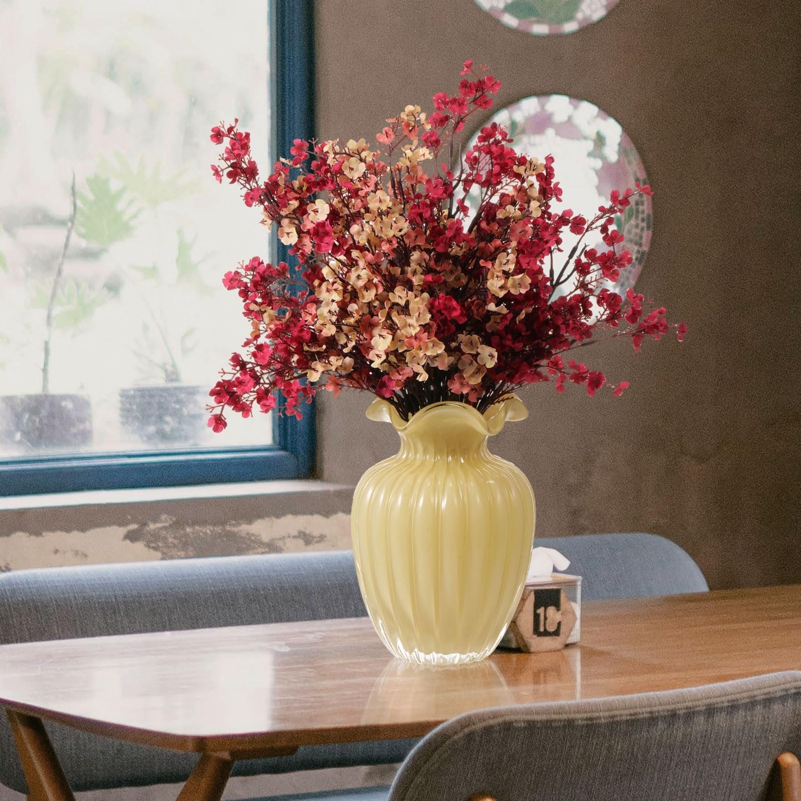 Artificial baby's breath flowers in coffee and burgundy colors arranged in a yellow vase on a wooden table.