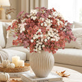 Bouquet of artificial baby's breath flowers in pink, white, and coral hues in a ribbed vase on a coffee table with decorative pumpkins and candles.