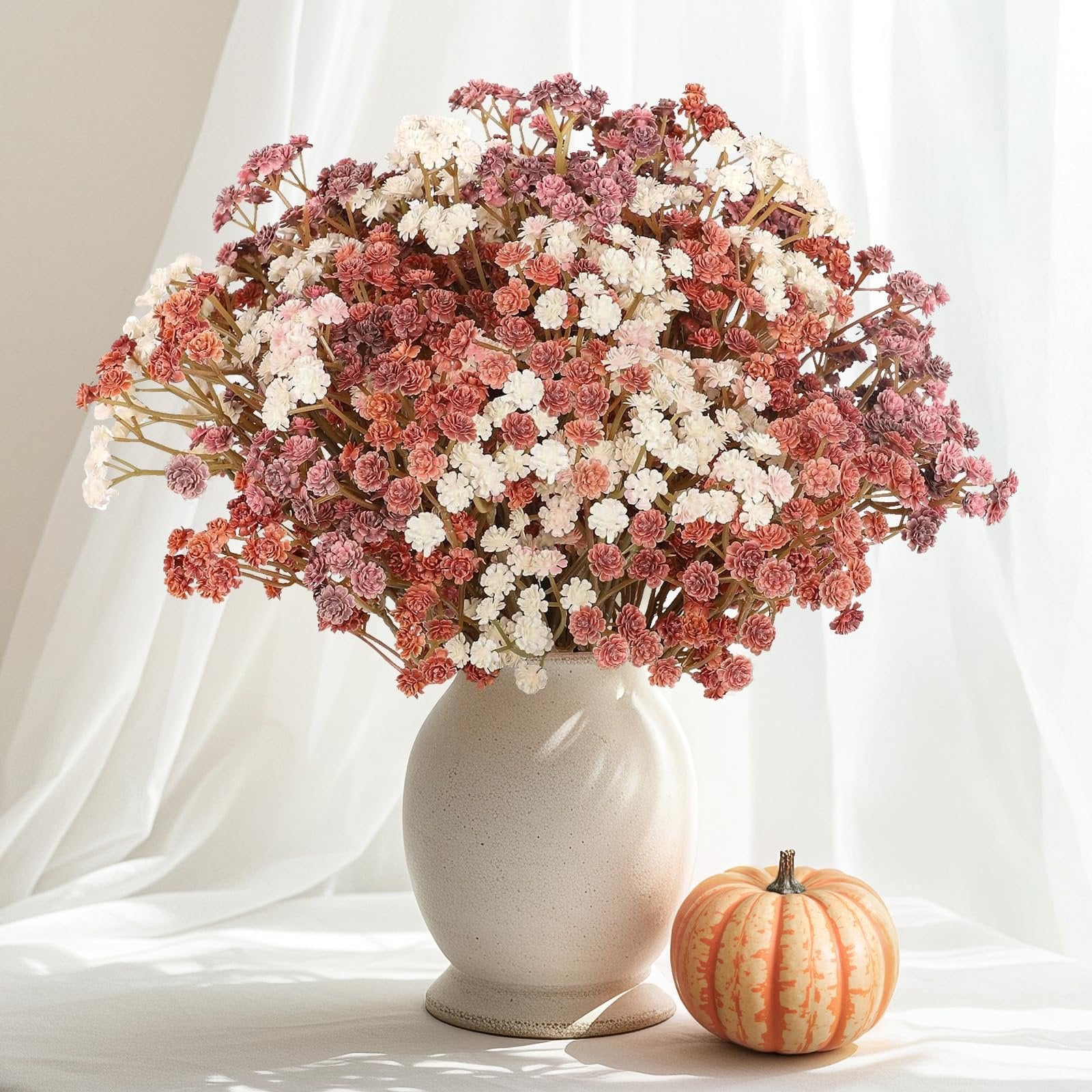 Bouquet of mixed pink, white, and coral artificial baby's breath flowers in a vase with a small pumpkin.