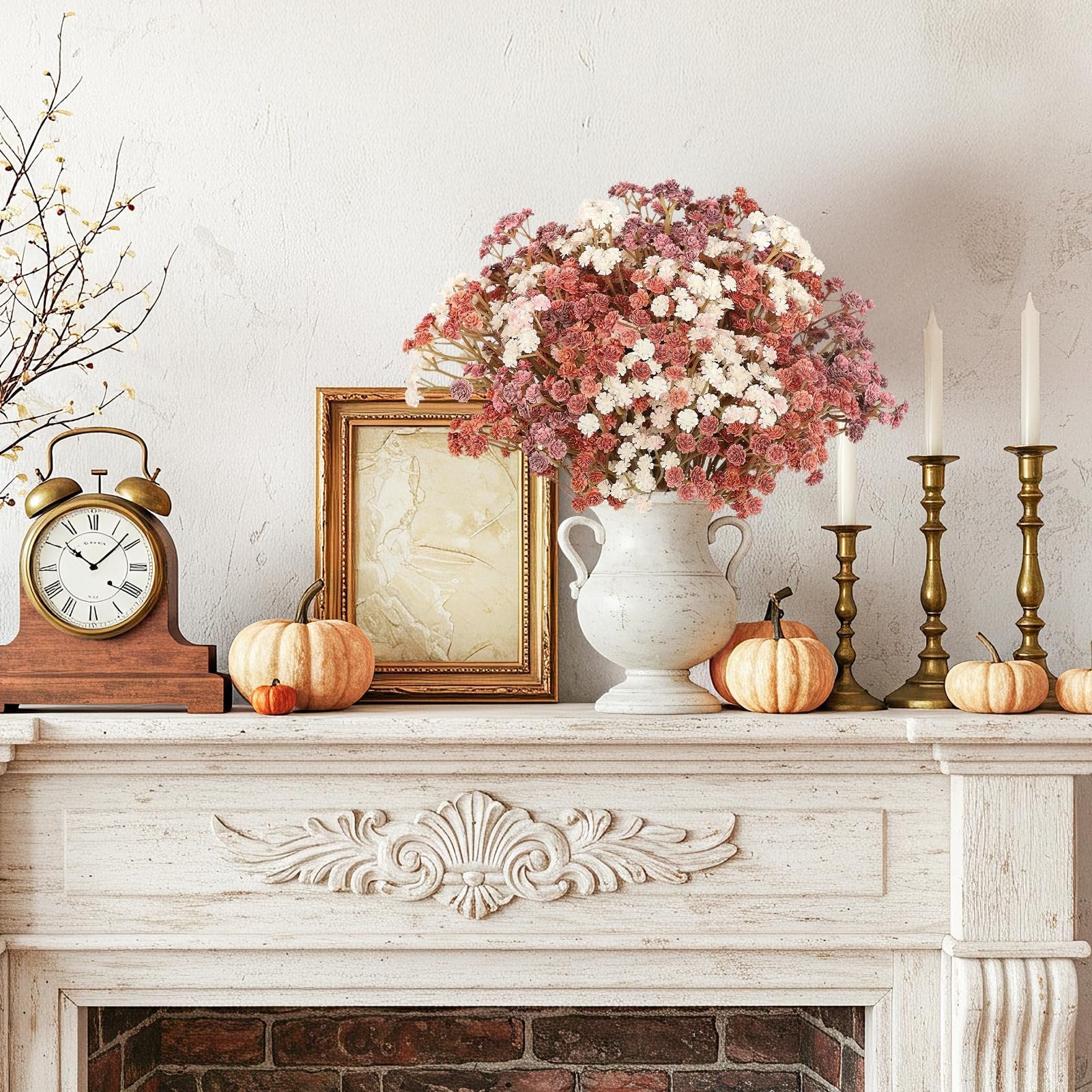 Fall mantelpiece decor with artificial baby's breath flowers in a vase, pumpkins, a clock, and candlesticks.
