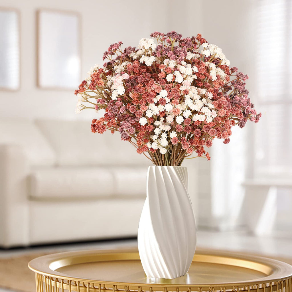 Bouquet of artificial baby's breath flowers in mixed pink, white, and coral hues, displayed in a white vase on a gold table.