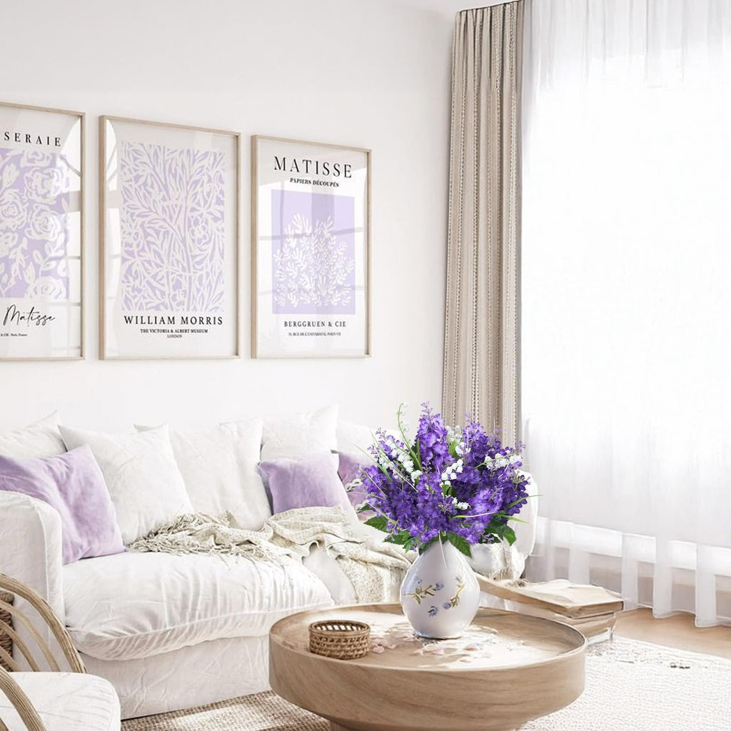 Artificial purple and white flowers in a vase on a coffee table in a living room with artwork on the wall.
