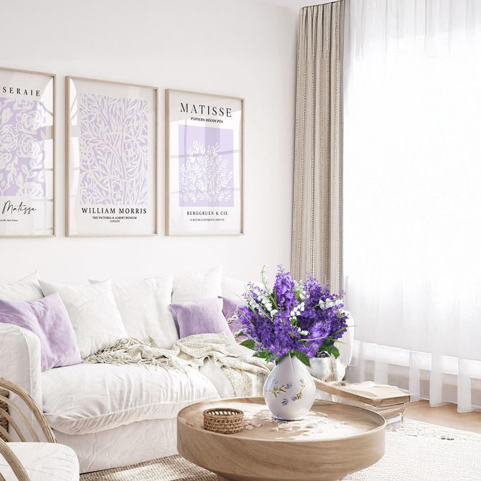 Artificial purple and white flowers in a vase on a coffee table in a living room with artwork on the wall.