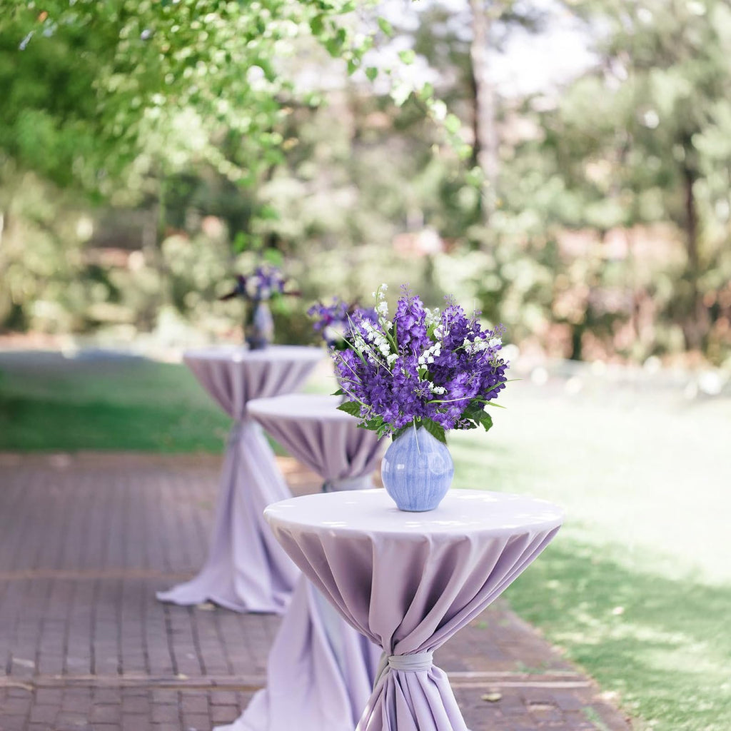 Purple and white artificial flower bouquet in a blue vase on a table at an outdoor event