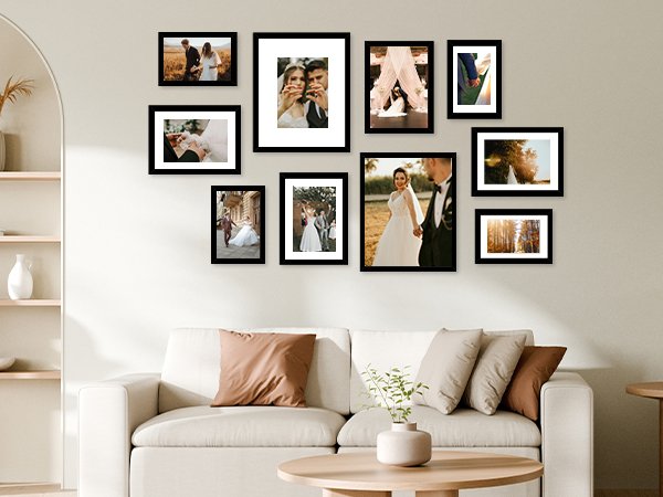 Collage of ten black picture frames displaying wedding photos on a wall above a sofa.