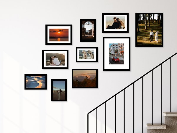 Collage of ten black picture frames displaying various scenic and couple photos on a white wall next to a staircase.