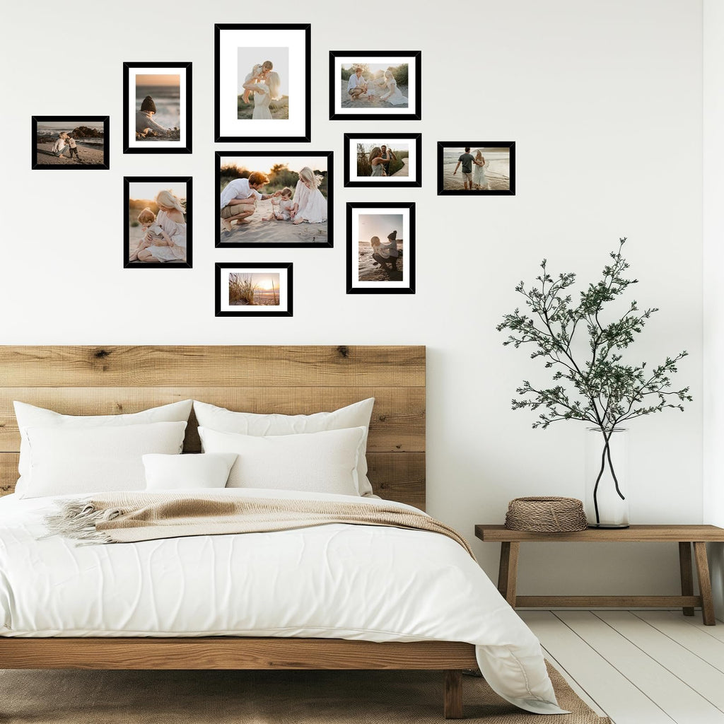 Collage of black picture frames displaying family photos on a white wall above a wooden bed.