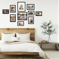 Collage of black picture frames displaying family photos on a white wall above a wooden bed.