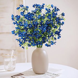 Bouquet of 10 blue baby's breath silk flowers in a beige vase on a table with a glass of water and newspaper.