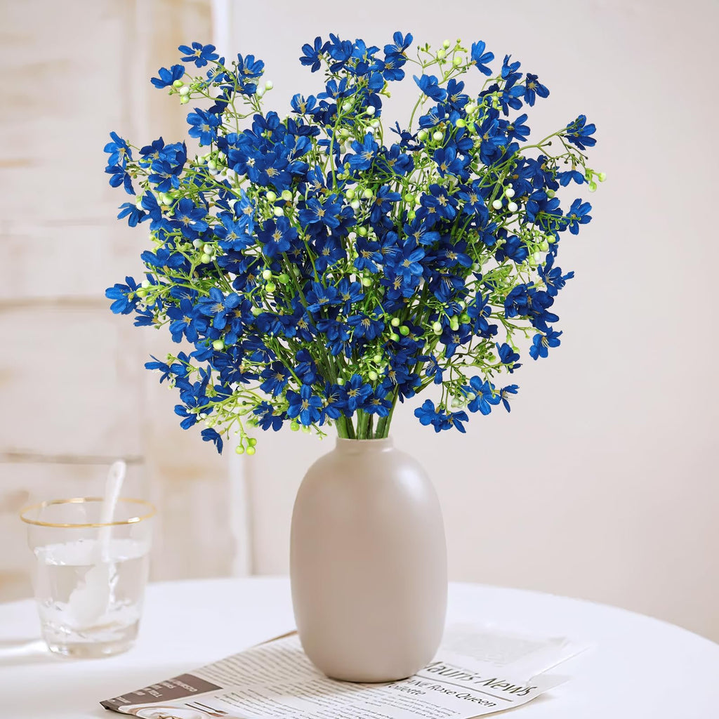 Bouquet of blue baby's breath silk flowers in a beige vase on a table with a glass of water and newspaper.